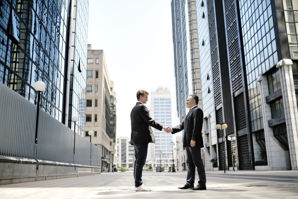 two businessmen shaking hands on background office corporate buildings
